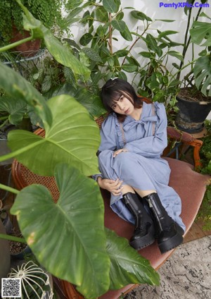 A woman sitting on a wicker chair in a room with plants.