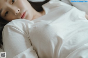 A woman in a white shirt is sitting on a bed.
