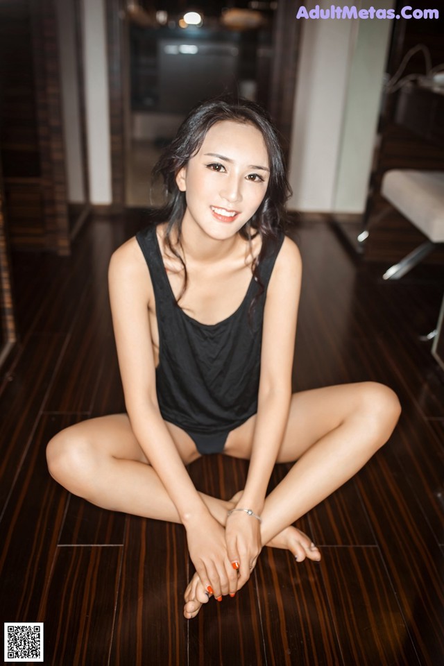 A woman sitting on the floor in a black bathing suit.