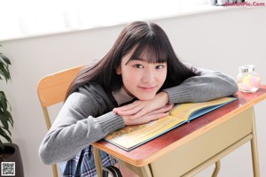 A young woman in a school uniform sitting on a desk.