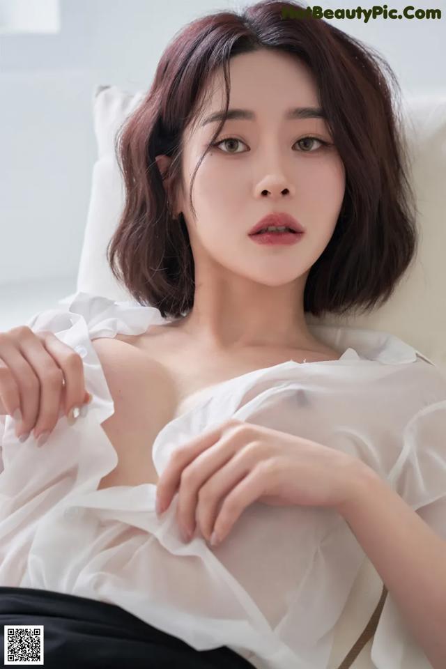 A woman in a white blouse sitting on a white couch.