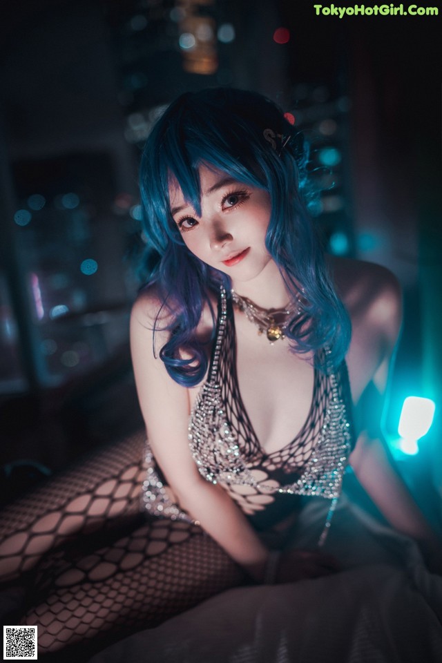 A woman with blue hair sitting on a bed.