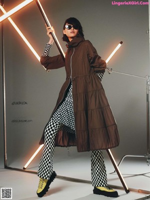 A woman in a green dress and brown coat holding a light saber.