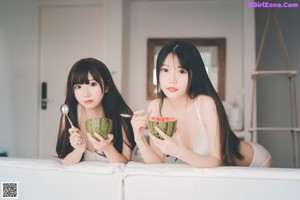 Two young women in underwear eating watermelon on a bed.